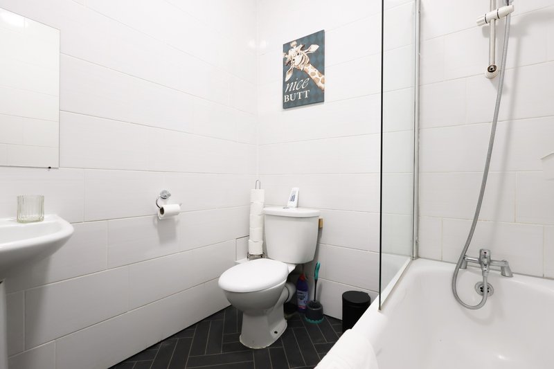 Clean bathroom with white tiles, toilet, sink, shower cubicle and black floor