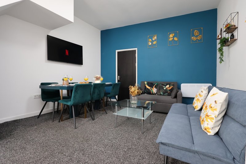 Open-plan living and dining area with blue accent wall, grey sofa, dining table and chairs