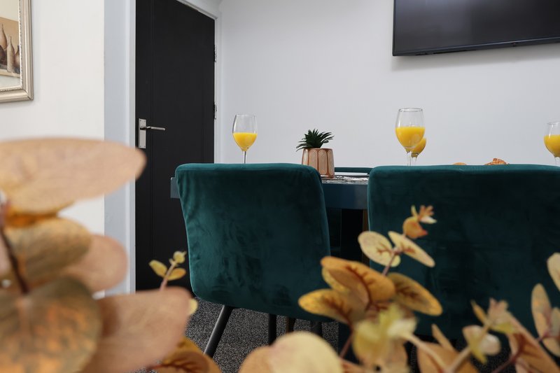 Modern dining area with teal chairs, table set with glasses, wall-mounted TV