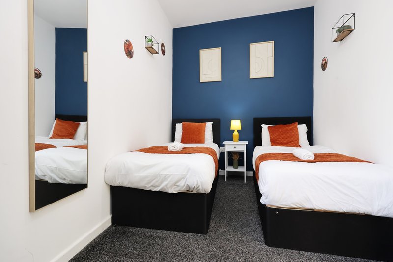 Twin bedroom with navy feature wall, white bedding, orange throws and wall-mounted decor