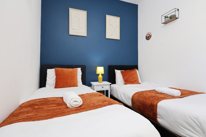 Twin bedroom with blue accent wall, orange cushions, white bedding and small side table