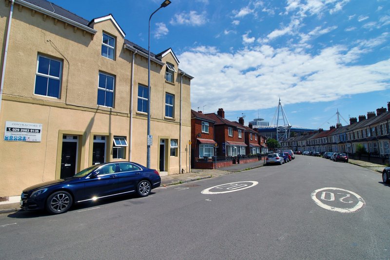 Cream-coloured period building with dark door and windows, street view with parked car and blue sky