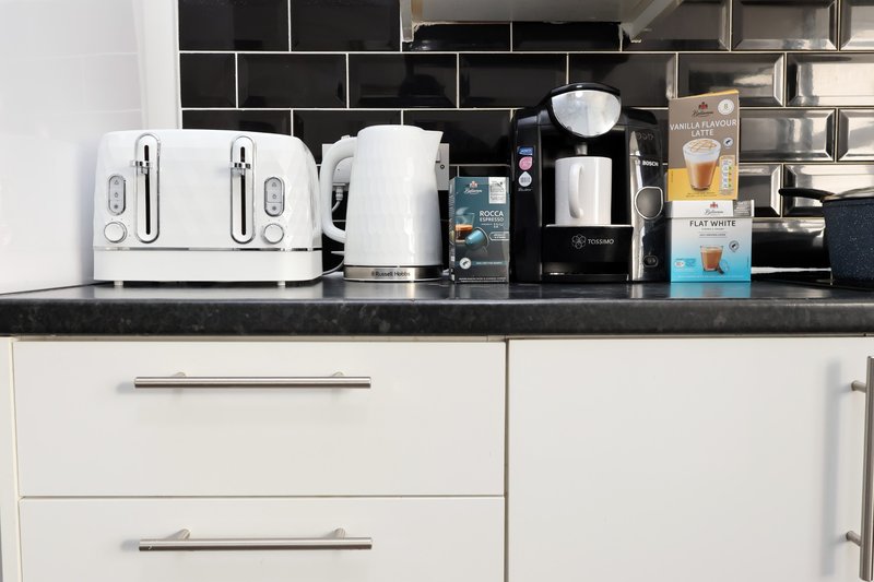 Modern kitchen counter with white appliances, kettle, and black subway tile backsplash