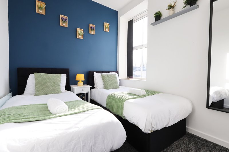 Twin bedroom with blue feature wall, white bedding, green accents and window
