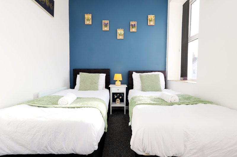 Twin bedroom with blue accent wall, two single beds, green bedding, and wall-mounted artwork