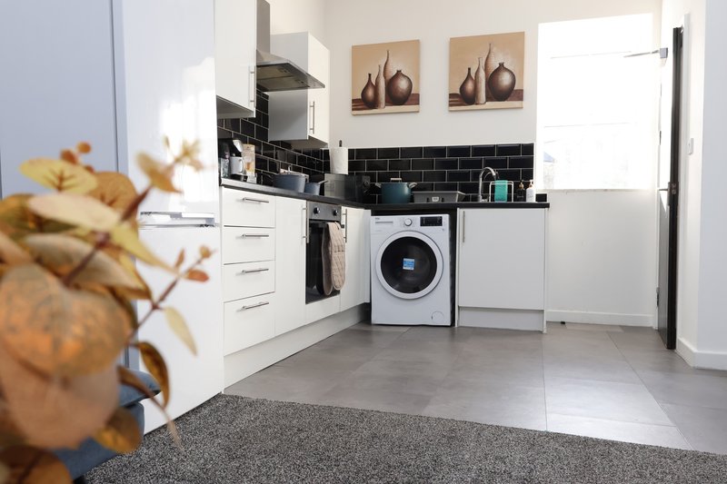 Modern kitchen with white cabinets, black tile backsplash, washing machine and stainless steel appliances