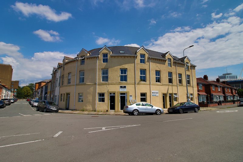 Yellow corner building with blue windows, street view with parked cars and clear sky