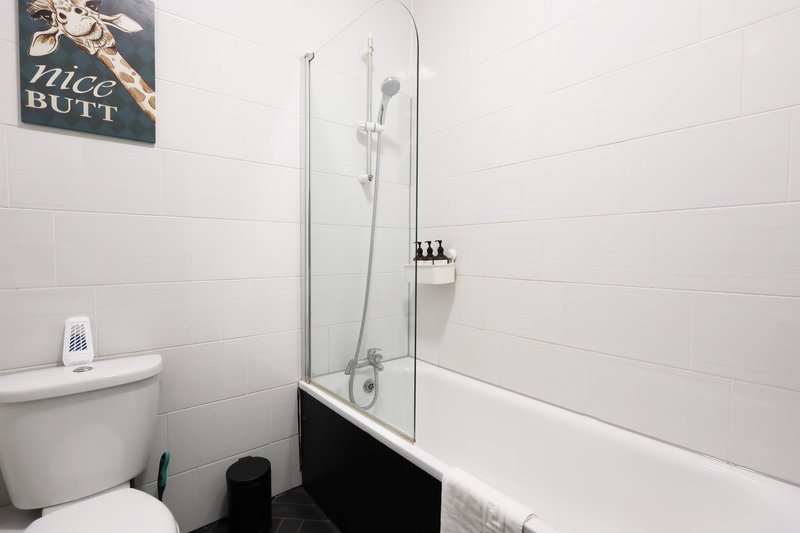 Clean bathroom with white tiles, toilet, bathtub with glass shower screen and shower fixtures