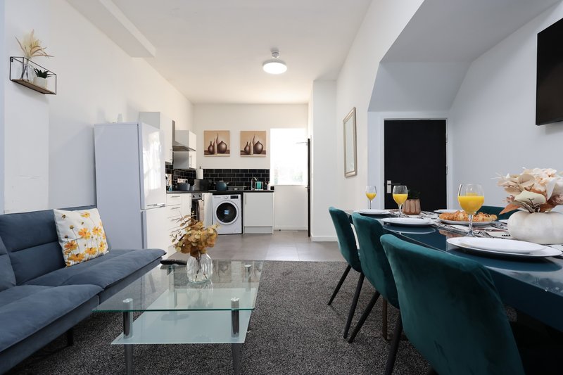 Open-plan living and kitchen area with blue sofa, dining table, washing machine and modern furnishings