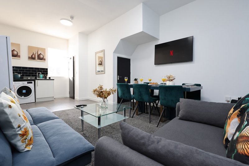 Open-plan living space with sofa, dining table, kitchenette, and mounted TV