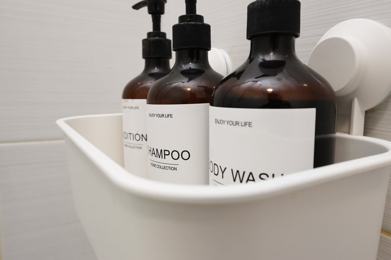 White bathroom caddy with shampoo, body wash, and lotion bottles in dark amber glass