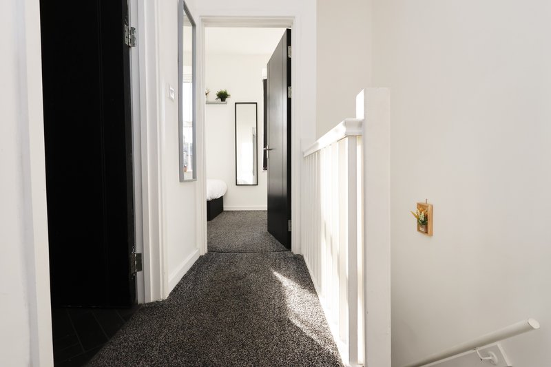 Bright hallway with gray carpet, white walls, dark doors, and natural light from window