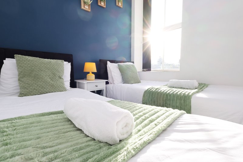 Modern bedroom with twin beds, green bedding, blue accent wall and window with natural light