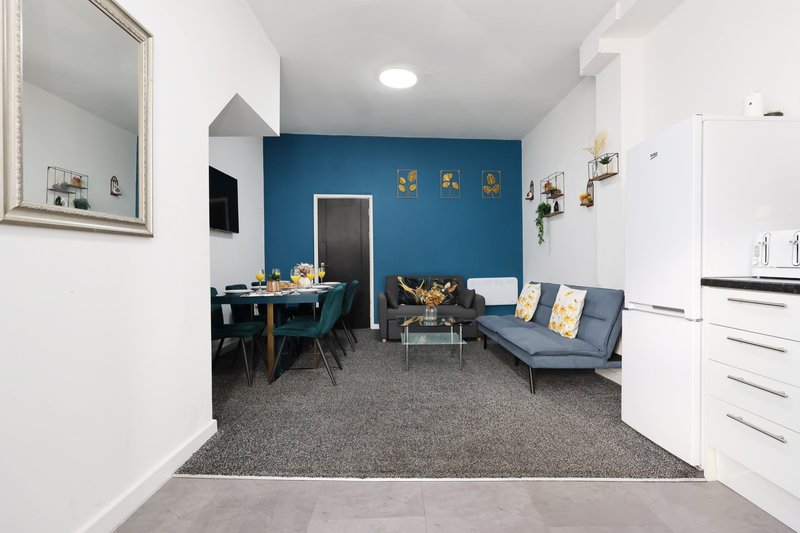 Open-plan living space with blue accent wall, dining table, sofa, and kitchen area