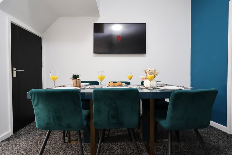 Modern dining room with teal velvet chairs, wooden table, wall-mounted TV, and place settings