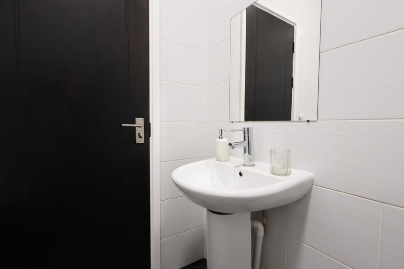 Modern bathroom with white pedestal sink, mirror cabinet, and black door