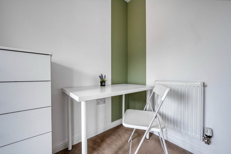 Small home office with white desk, folding chair, green accent wall and radiator