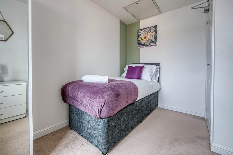 Compact bedroom with single bed, purple bedding, white pillows and small dresser