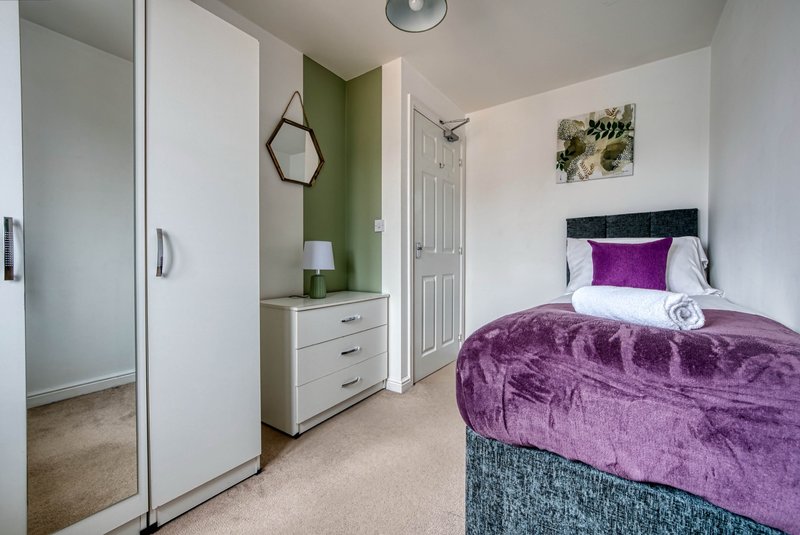 Bedroom with double bed, purple bedding, wardrobe, dressing table and green accent wall