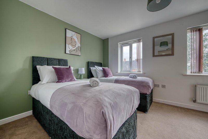 Bright bedroom with two single beds, green accent wall, windows and framed artwork