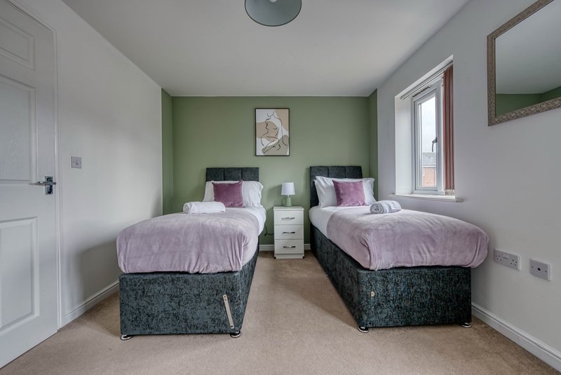 Twin bedroom with two single beds, green accent wall, bedside tables and windows