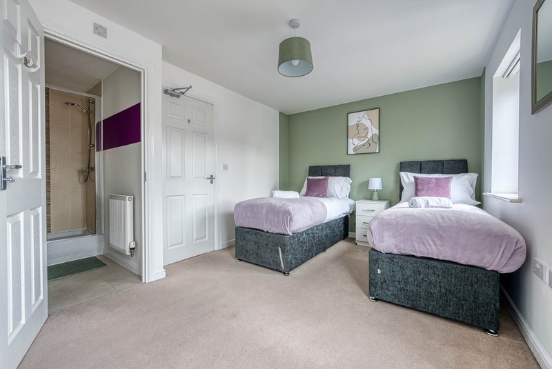 Spacious bedroom with two single beds, sage green wall, ensuite bathroom and large windows