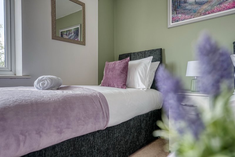 Bedroom with double bed, purple bedding, decorative pillows, and potted flowers in foreground