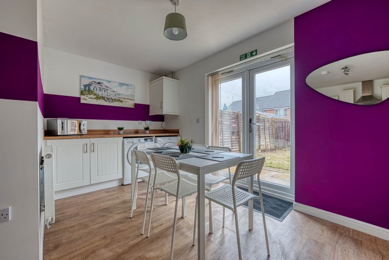 Modern kitchen-diner with purple accent wall, white cabinetry, dining table and glass doors to garden