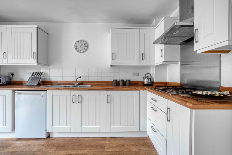 Modern white kitchen with wooden worktops, gas cooker, stainless steel hood and wall clock