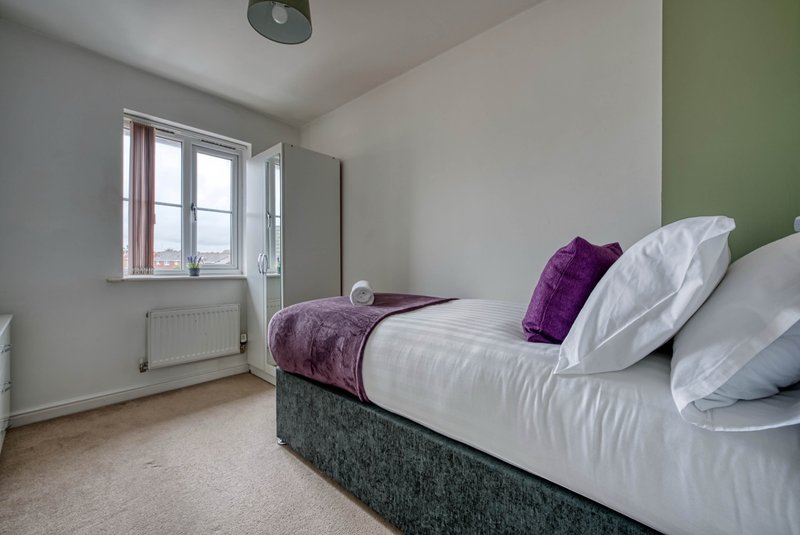 Bright bedroom with double bed, purple cushions, white pillows, window and green accent wall