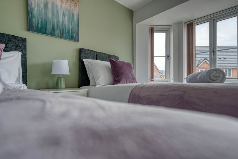 Modern bedroom with twin beds, green accent wall, bedside lamp and street-facing windows