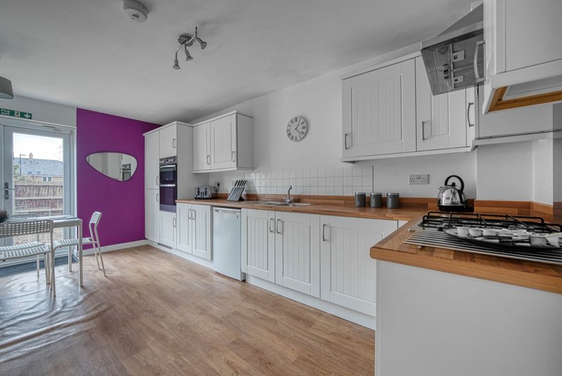 Modern kitchen with white cabinetry, wooden worktops, gas hob and purple accent wall