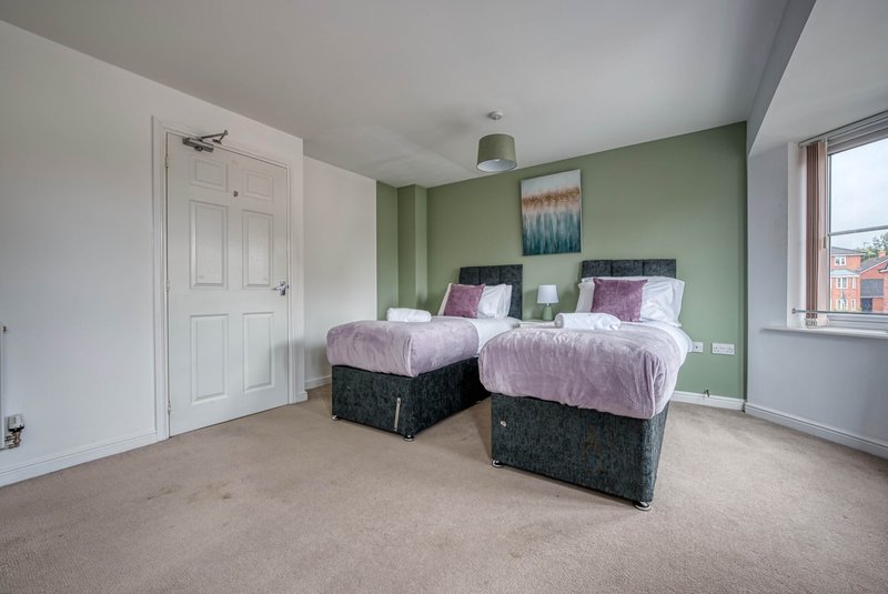 Bedroom with two single beds, purple bedding, green accent wall, and window with city view