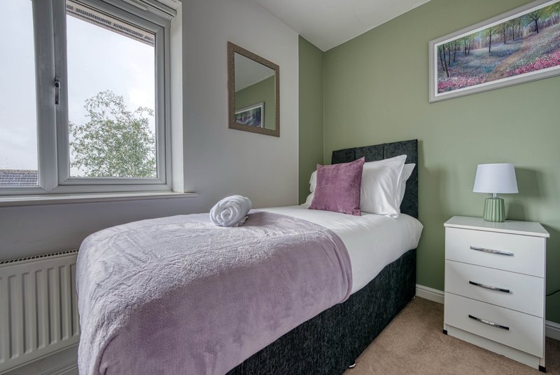 Bedroom with double bed, pink bedding, white nightstand, green walls and window