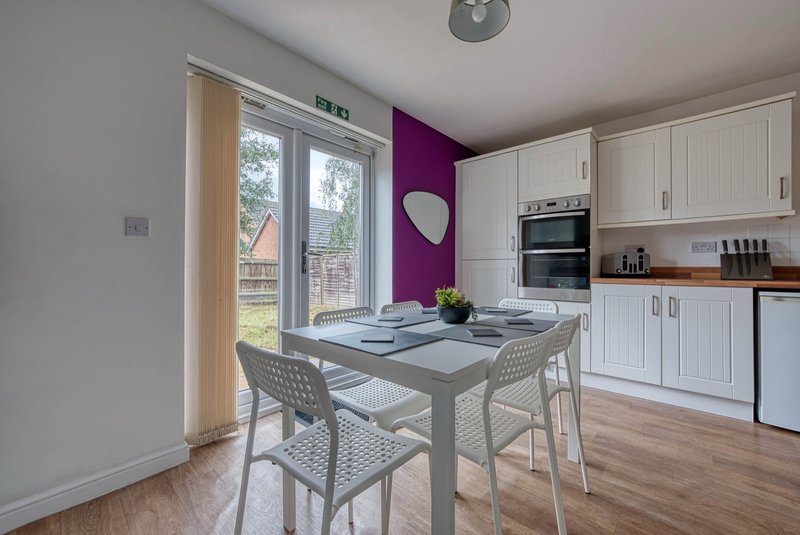 Modern kitchen with dining table, white cabinetry, purple accent wall and garden view