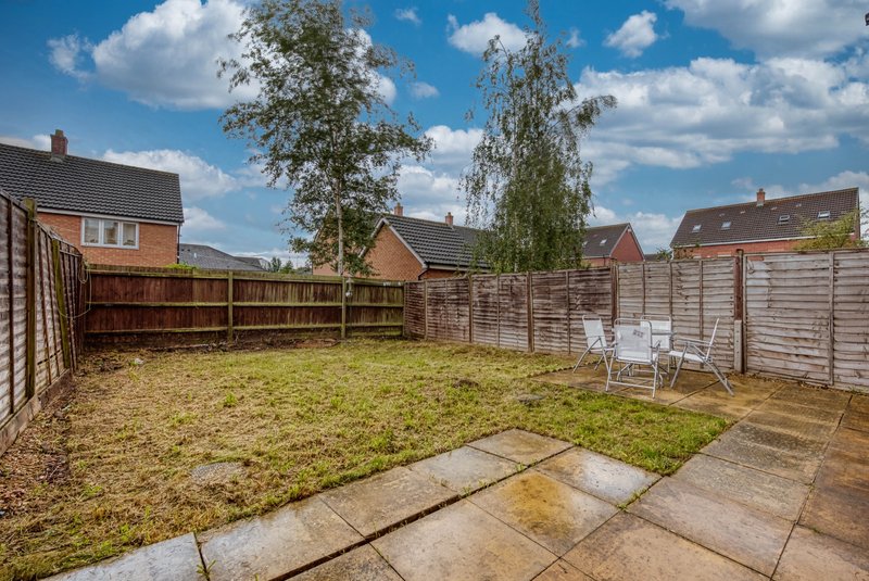 Residential garden with paved patio, lawn, wooden fences and neighbouring houses