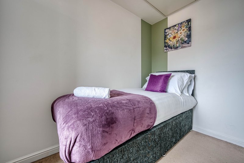Bedroom with single bed, purple velvet bedding, white pillows and wall art
