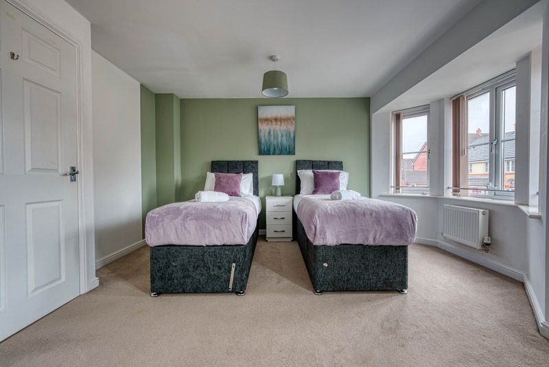 Bright bedroom with two single beds, green accent wall, and large windows overlooking street