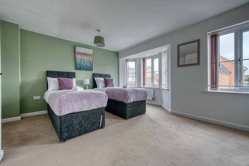 Bright bedroom with two single beds, green accent wall, purple bedding and windows with views