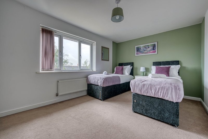 Bright bedroom with two single beds, green accent wall, large window and pendant light
