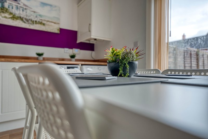 Modern kitchen with white dining table, purple accent wall, and window view