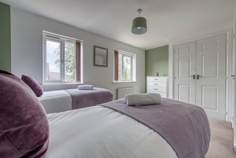 Spacious bedroom with two beds, purple cushions, windows, wardrobe and pendant light
