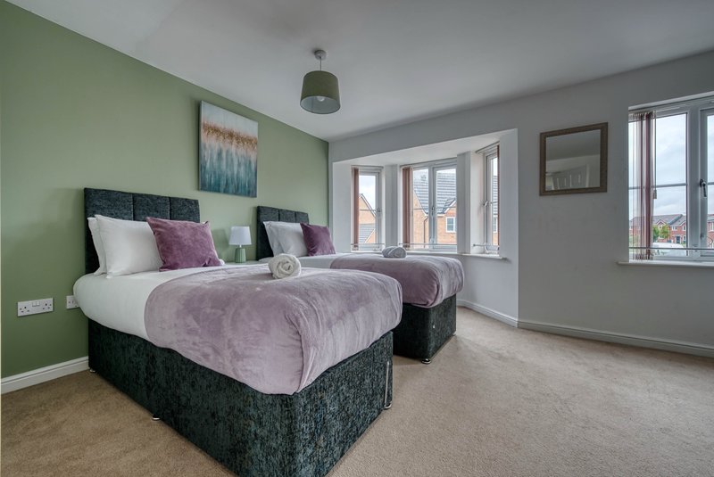 Bright bedroom with two double beds, green wall, purple bedding, windows and grey carpet