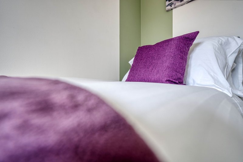 Bedroom with purple cushion, white pillows and green accent wall