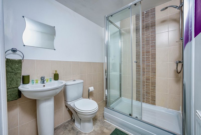 Clean bathroom with pedestal sink, toilet, shower enclosure and tiled walls