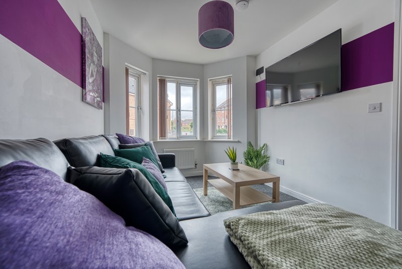 Modern living room with purple and grey accents, sofa, wooden coffee table, and bay window