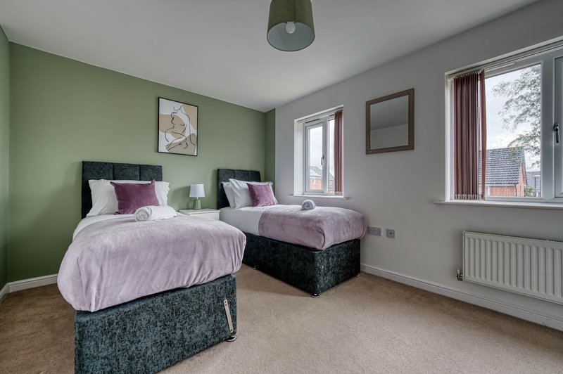 Twin bedroom with two single beds, green accent wall, windows with curtains and radiator
