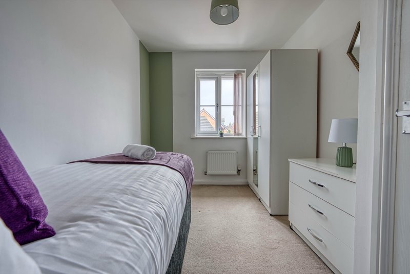 Bedroom with single bed, white dresser, wardrobe and window with radiator