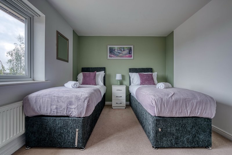 Twin bedroom with two single beds, purple bedding, green accent wall, window and bedside table