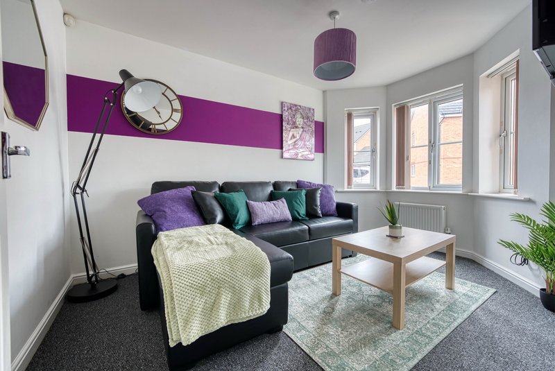 Modern living room with dark sofa, purple and teal cushions, wooden coffee table, and large windows